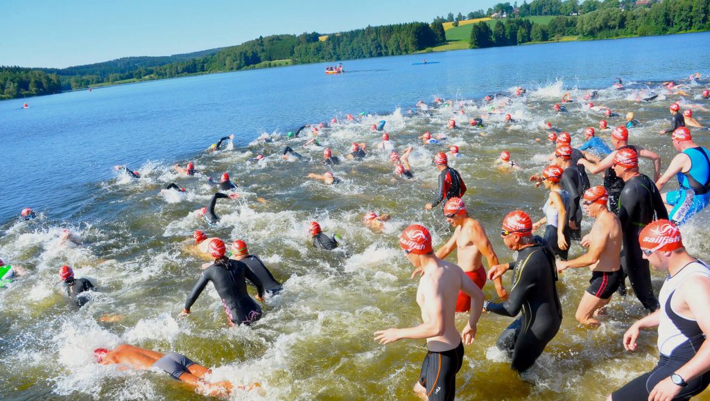 Zu sehen sind viele Triathleten die durch einen See schwimmen